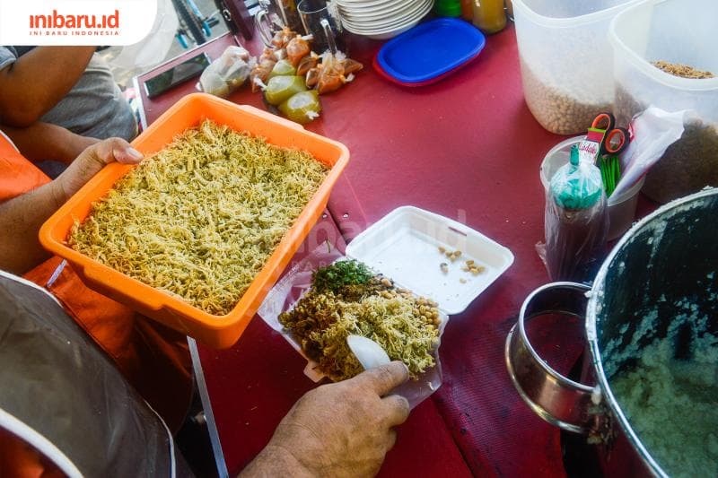 Mang Dede sedang menambahkan topping ayam untuk bubur pesanan pelanggan yang dibungkus. (Inibaru.id/ Kharisma Ghana Tawakal)