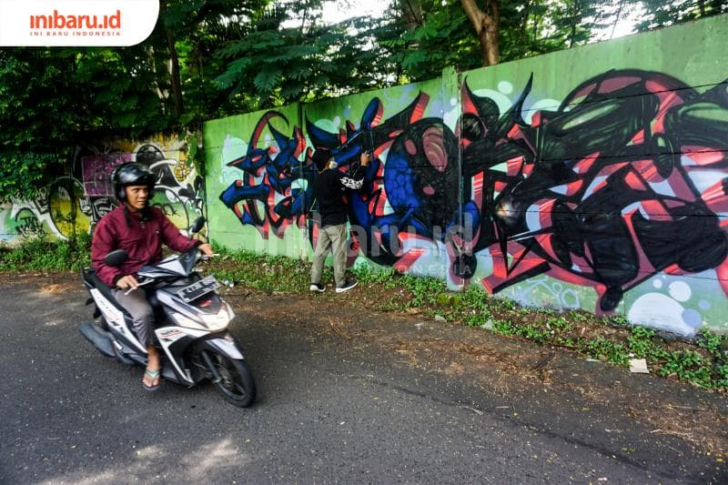 Seorang pengendara sepeda motor sedang melintas saat anggota Bring No Clan membuat grafiti. (Inibaru.id/ Audrian F)<br>