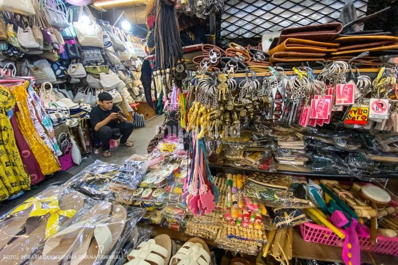 Seorang pedagang yang terlihat santai bermain gawai menunggu wisatawan datang.