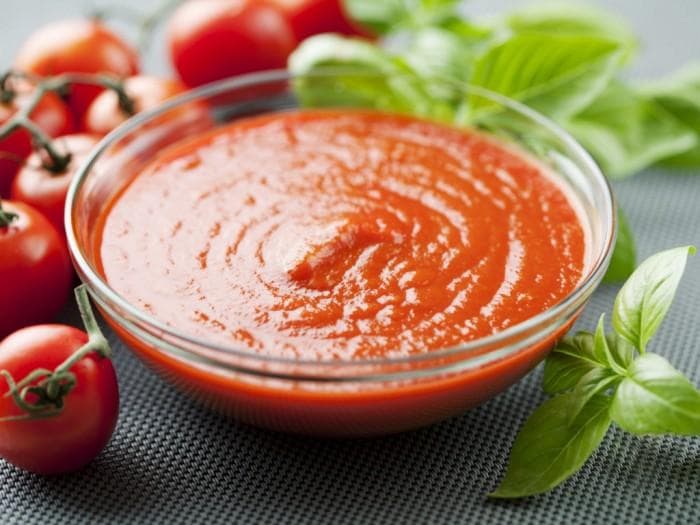 Mangkuk saus tomat segar dengan daun basil di atasnya, menunjukkan warna merah cerah dan tekstur kental yang sempurna untuk pasta
