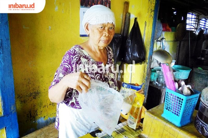 Tuminem atau yang kerap dipanggil Bu Sujud sedang menunjukkan berbagai macam bahan-bahan makanan di warungnya seperti beras, gula, dan minyak. (Inibaru.id/Isma Swastiningrum)
