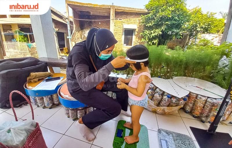 Petugas posyandu sedang mengecek berat badan seorang anak perempuan. (Inibaru.id/ Fitroh Nurikhsan)