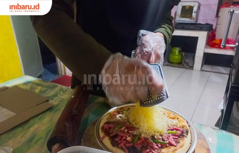 Proses pemberian topping pada adonan pizza sebelum di oven. (Inibaru.id/ Fitroh Nurikhsan)