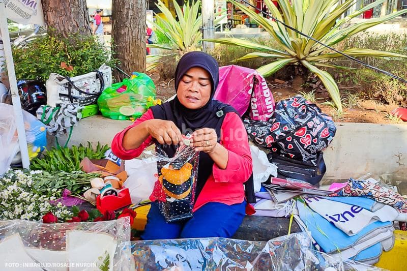 Seorang penjual buket tengah membungkus buket boneka beruang coklat buatannya.