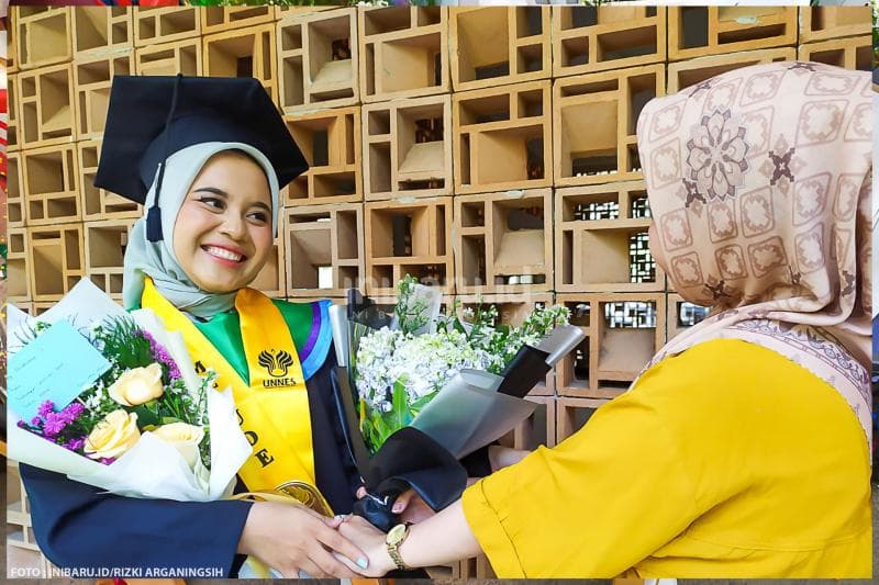 Senyum bahagia seorang wisudawan ketika menerima buket bunga dari temannya.&nbsp;