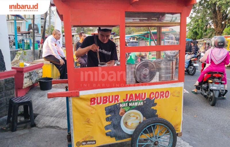 Muhammad Latif Awaludin tengah melayani pembeli di balik gerobak bubur jamu coro miliknya yang terparkir di Jalan Bhayangkara, Kecamatan Kota, Kabupaten Demak. (Inibaru.id/ Ayu Sasmita)