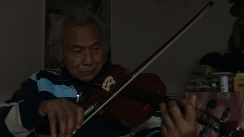 Asahan Aidit, adik bungsu D. N. Aidit yang tinggal di Belanda, tengah mencoba biola lama milik anaknya. (Arsip Lola Amaria Pictures, Kompas.id)