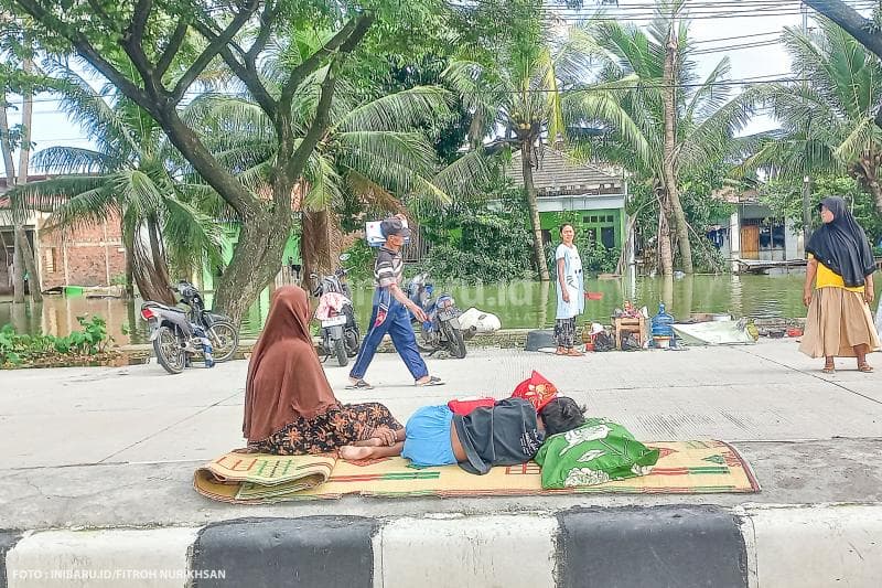 Seorang anak kecil sedang tertidur pulas di pembatas jalan Pantura Demak-Kudus ditemani oleh orang tuanya.