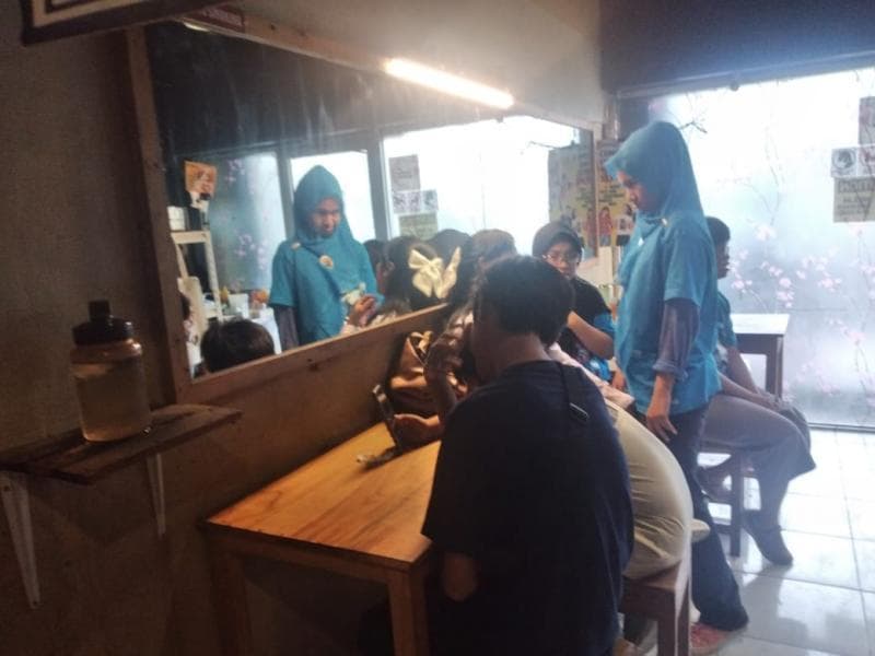 Pelayan disabilitas berseragam biru tengah memberikan servis dengan menyodorkan menu makanan kepada pengunjung restoran wasabi di Jalan MGR Soegijapranata, depan Pasar Bulu Semarang. (Inibaru.id/Danny Adriadhi Utama)