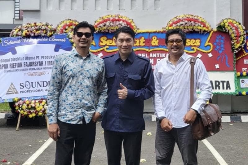 Berlatar deretan karangan bunga, Ifan (tengah) tampak berdiri di depan Gedung PFN bersama dua rekannya. (Instagram/ivolks_creative via Kompas)