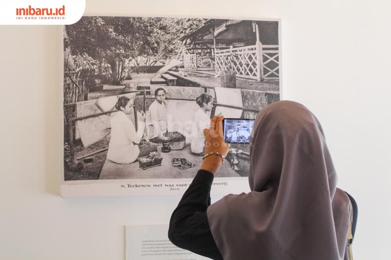 Seorang pengunjung sedang mengabadikan foto lama tentang karya batik dipamerkan. (Inibaru.id/Imam Khanafi)