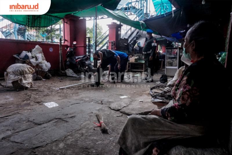 Seorang pedagang menyaksikan para petugas yang sedang membuat pemetaan jarak di lokasi lapaknya. (Inibaru.id/ Audrian F)<br>