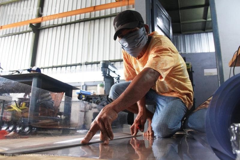 Pekerja memotong mika yang digunakan dalam pembuatan face shield.