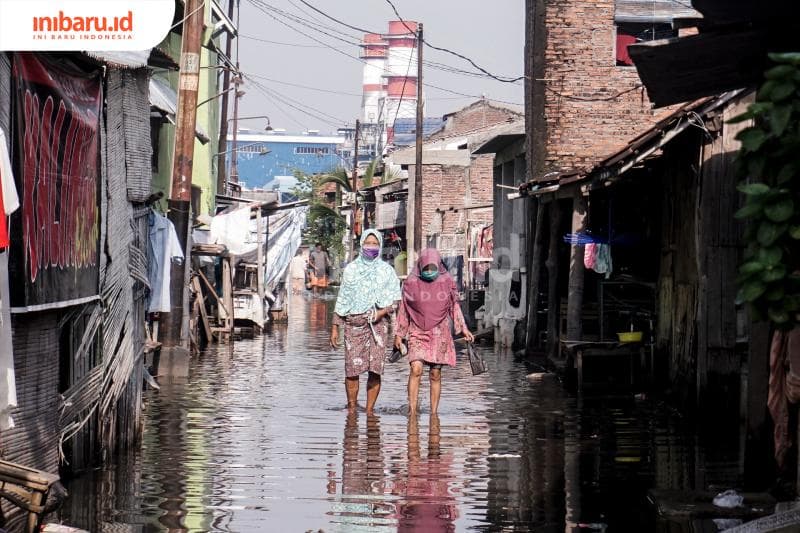 Warga Tambaklorok melintas di tengan kepungan air. Mereka memilih pasrah dengan banjir rob Semarang. (Inibaru.id/ Audrian F)<br>
