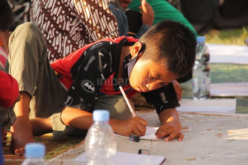 Di posko pengungsian, seorang anak terlihat serius menggambar bersama para sukarelawan.<br>