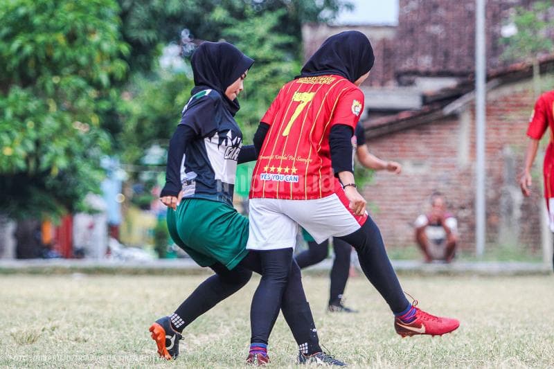 Dua pemain perempuan berebut bola di sebuah lapangan sepak bola kampung.