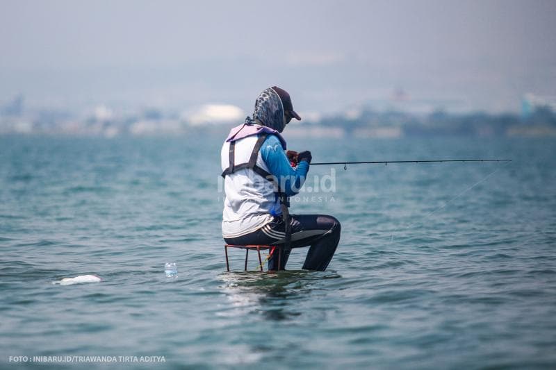Seorang pemancing yang duduk di atas kursi di tengah laut, dekat dengan Dam Ijo Semarang.