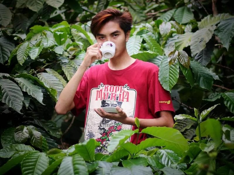 Muh Azharuddin alias Aan meneguk kopi khas lereng Muria di kebun kopinya. (Instagram/Kopikampoengjrahi)