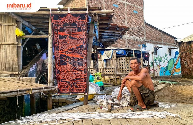 Nasoka, seorang nelayan yang sedang membuat tali untuk rumpon di laut nggak jauh dari karya seni yang ditampilkan dalam pameran Penta Klabs IV di Tambakrejo Semarang. (Inibaru.id/ Kharisma Ghana Tawakal)
