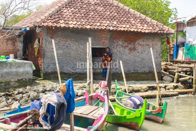Pasijah, satu-satunya keluarga yang tersisa di Kampung Senik, berdiri di belakang rumahnya yang telah dikepung lautan.