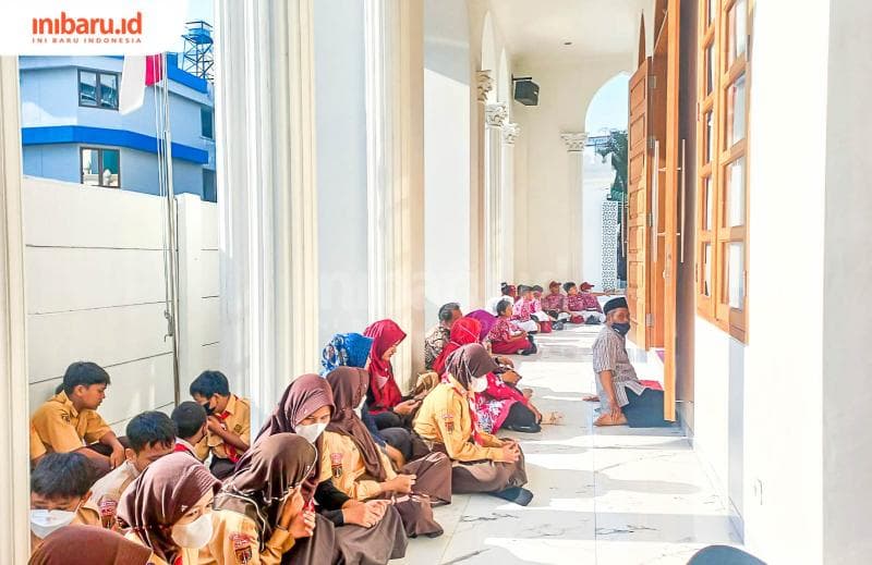 Para siswa dan guru SD di Kelurahan Kembangsari duduk di halaman luar makam Mbah Depok Semarang. (Inibaru.id/ Fitroh Nurikhsan)