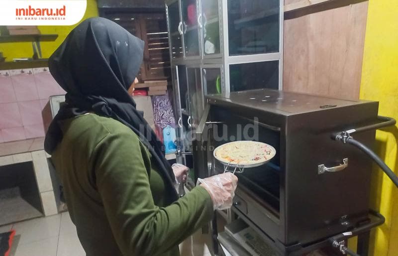 Feni Murdiyanti ketika hendak memasukan adonan piza yang telah ditaburi topping ke dalam oven. (Inibaru.id/ Fitroh Nurikhsan)
