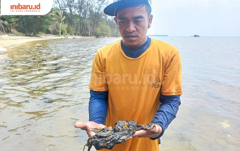 Seorang nelayan memperlihatkan lumut hitam yang mencemari Pantai Cemara. (Inibaru.id/ Fitroh Nurikhsan)